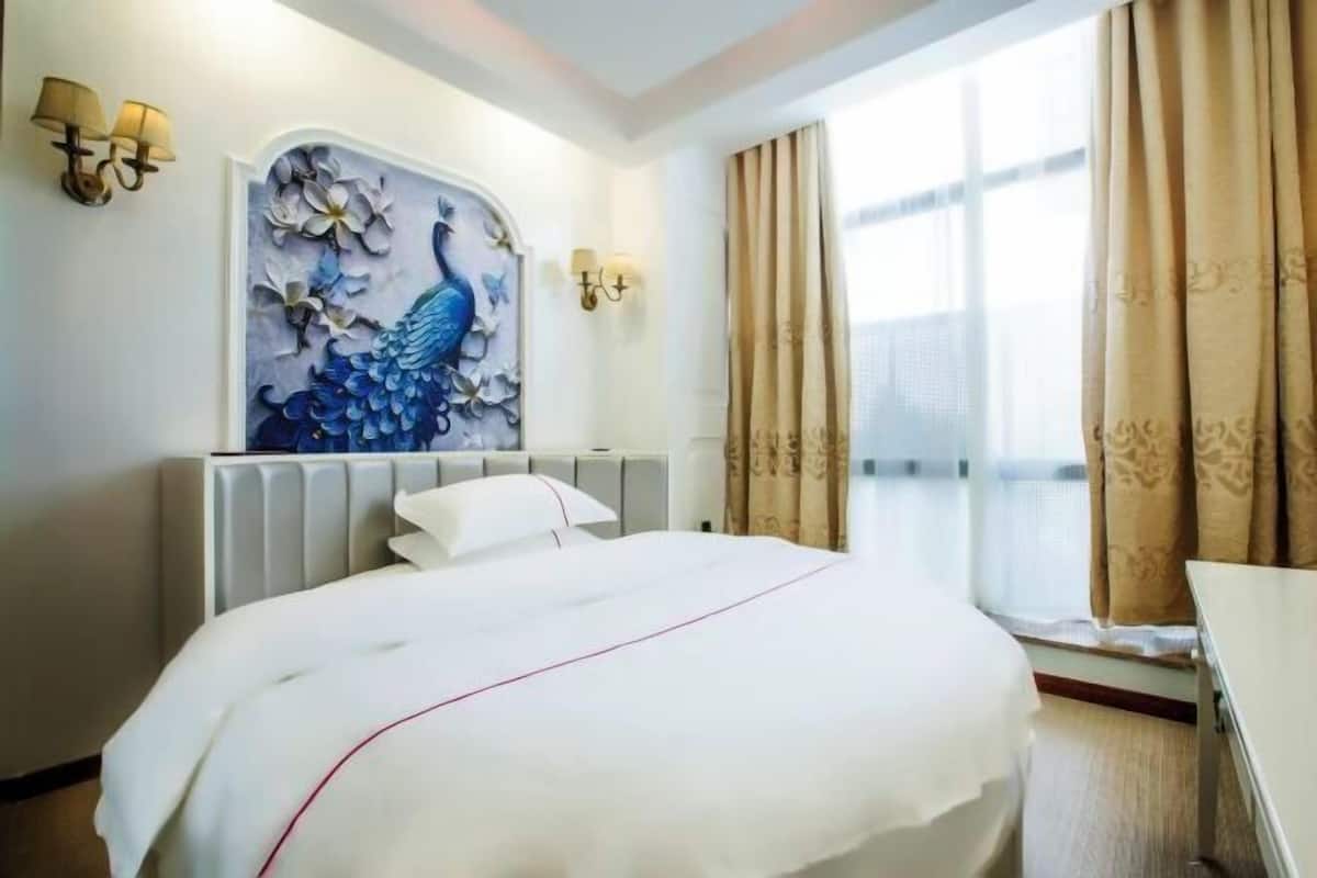 Une chambre d’hôtel avec un grand lit, un tableau représentant un paon accroché au mur, un radiateur et une fenêtre avec des rideaux.