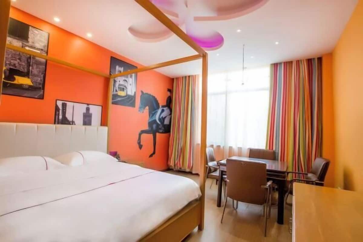 Une chambre d’hôtel avec un lit, une table à manger, des chaises, un rideau rayé aux couleurs vives et un mur orné de tableaux encadrés.