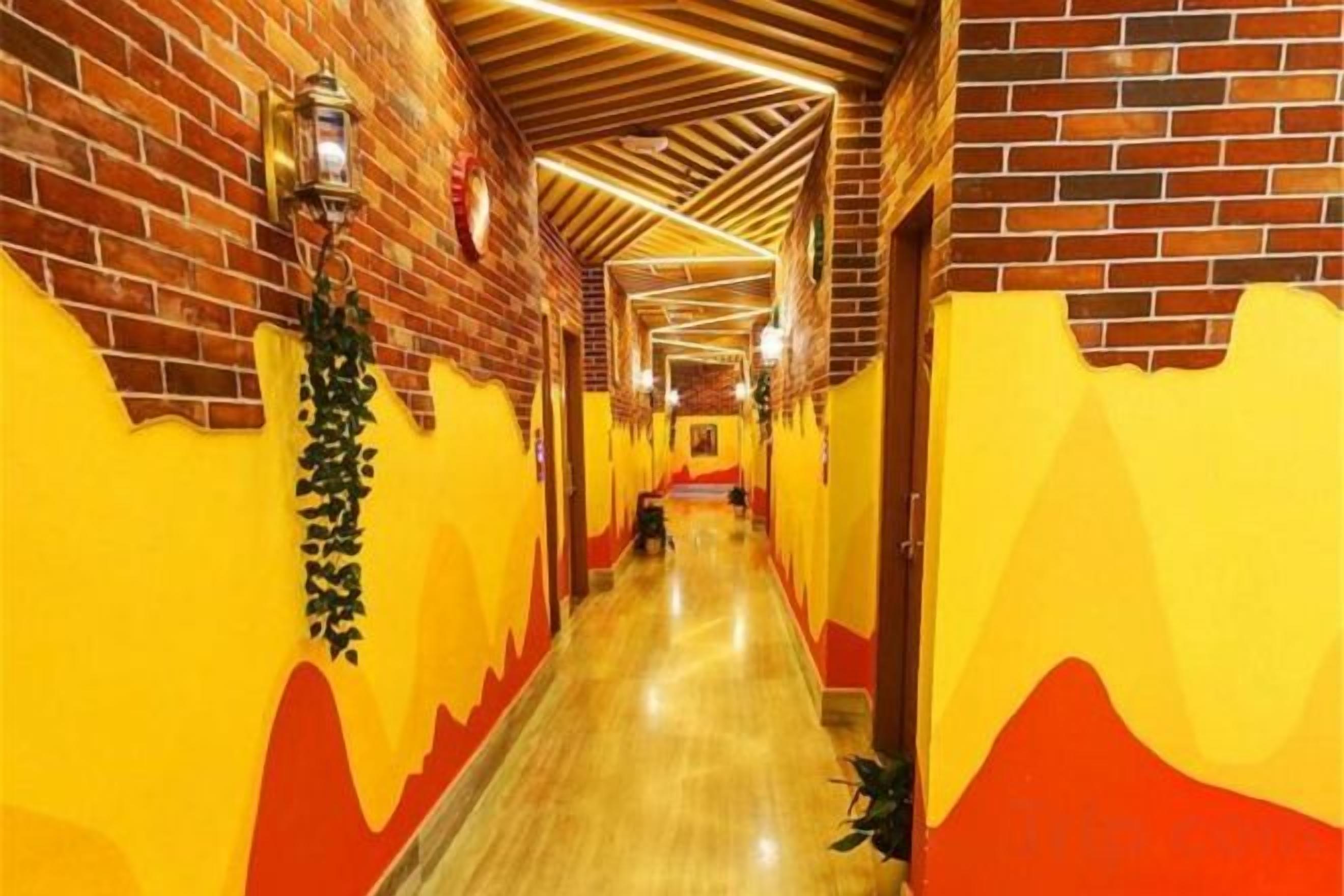 A corridor with brick walls and yellow and red painted walls, leading to a door at the end.