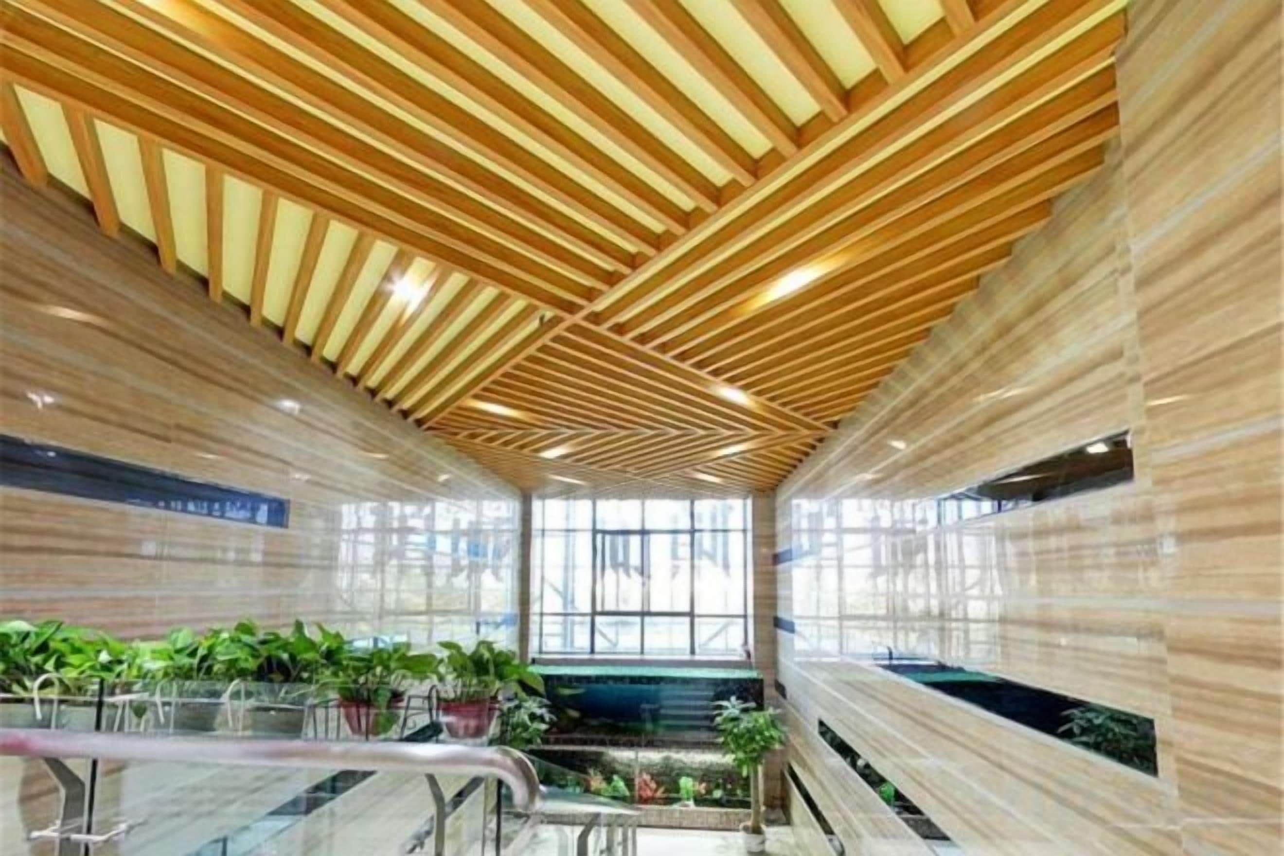 Un interior moderno con techo de listones de madera, barandales de vidrio y plantas de interior.
