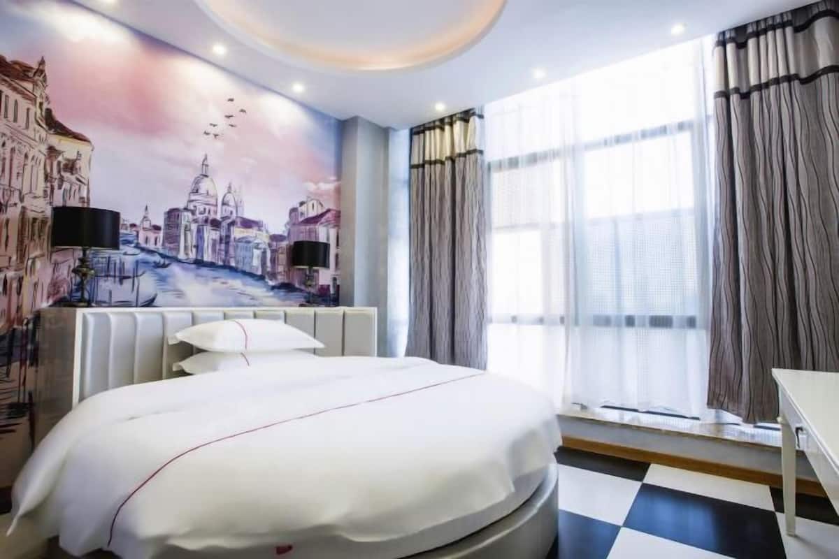 Une chambre d’hôtel avec un lit, une fresque représentant un paysage urbain, une fenêtre avec des rideaux et un sol à carreaux.