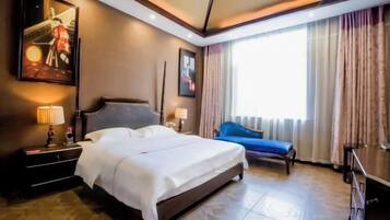 A hotel room with a bed, bedside tables, a nightstand, a blue sofa, a window with curtains, and artwork on the walls.