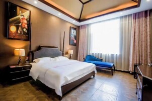 Una habitación de hotel con una cama, mesitas de noche, un sofá azul, una ventana con cortinas y obras de arte en las paredes.
