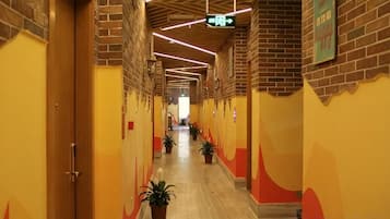 A corridor with brick walls, wooden doors, and potted plants.