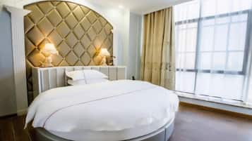 A modern bedroom with a tufted headboard, a round bed, bedside lamps, and a large window.