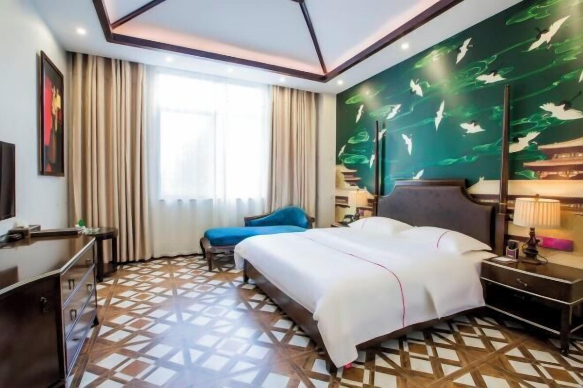 A hotel room with a large bed, a desk, a chair, and a patterned floor.