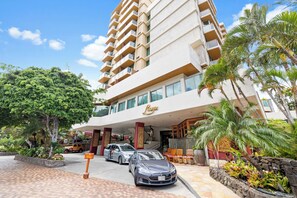 Een hotel met een modern ontwerp, met een opvallende entree, een parkeerplaats met auto's en weelderige tropische beplanting.