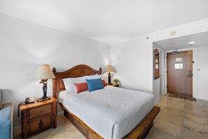 Una habitación de hotel con cama, lámparas de noche, mesita de noche y una puerta de madera.