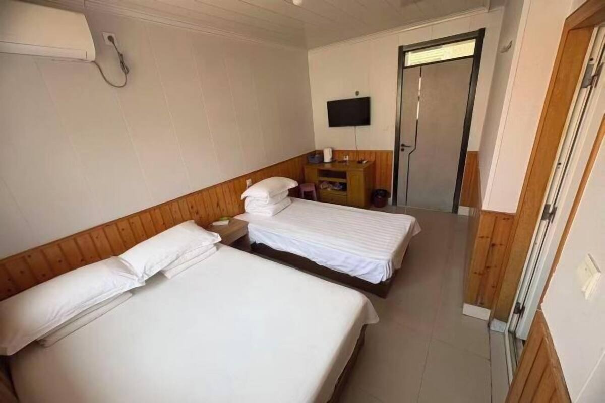 Ein Hotelzimmer mit zwei Betten, einem Fernseher, einem Holzkopfende, einem kleinen Tisch und einer Tür.