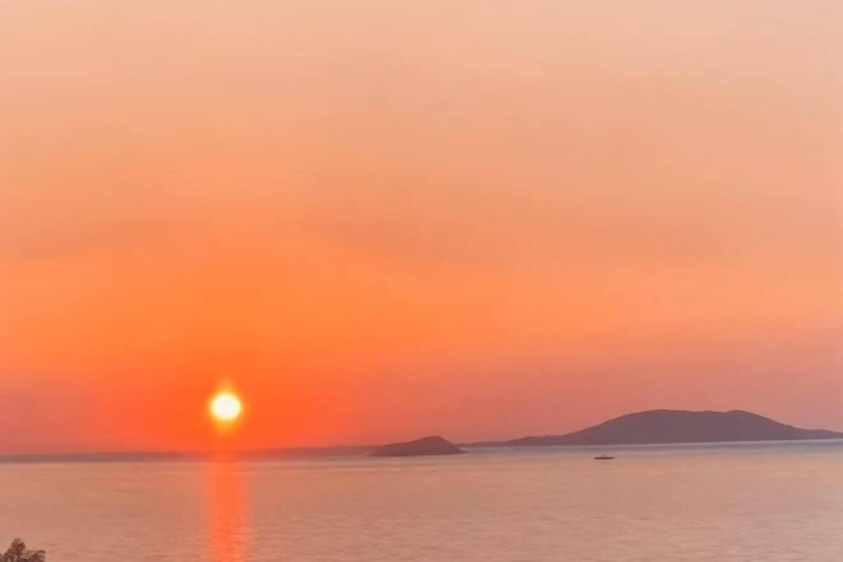Ein Sonnenuntergang über einem ruhigen Meer mit weit entfernten Landformen.