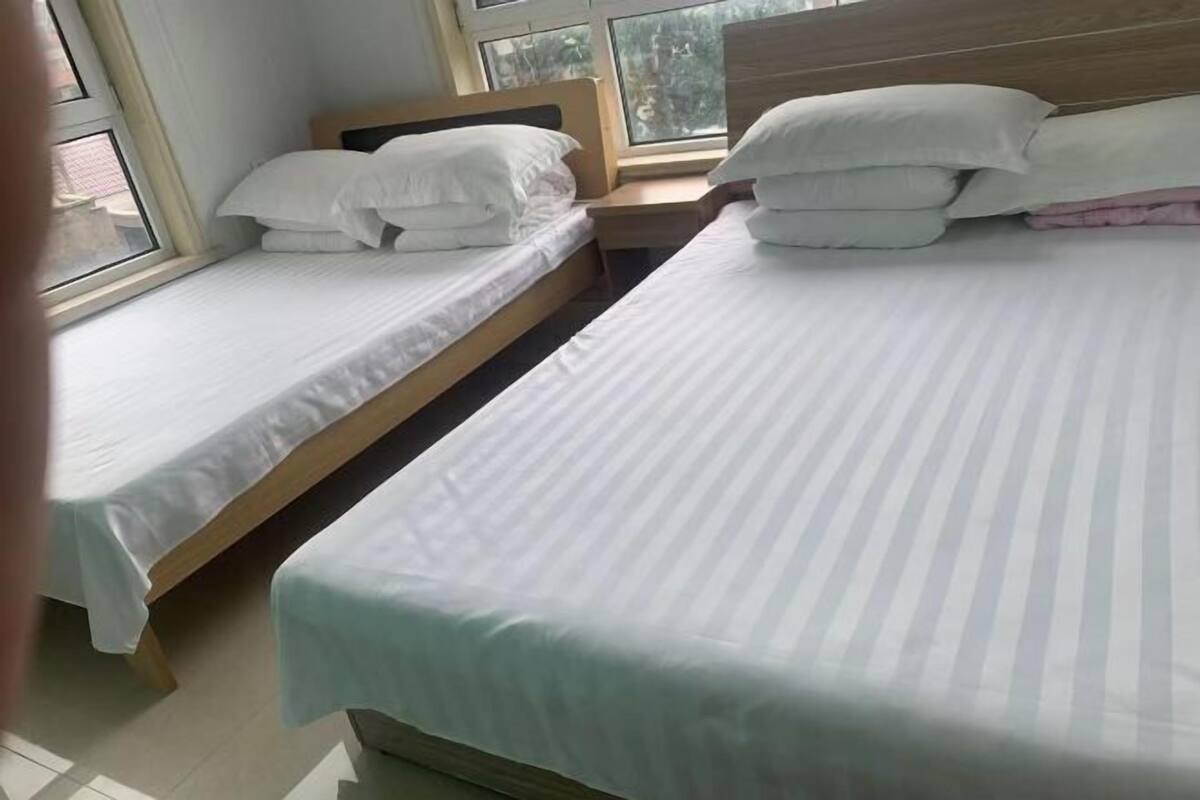 Ein Hotelzimmer mit zwei Einzelbetten, einem Holzkopfende und einem Fenster mit Blick auf Bäume.