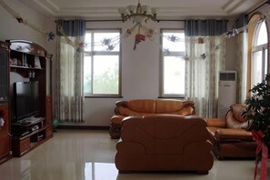 A living room with a sofa, a television, and a bookshelf. - Qingdao Lushan Shanhai Yihai Guanhai Hotel (Qingdao)