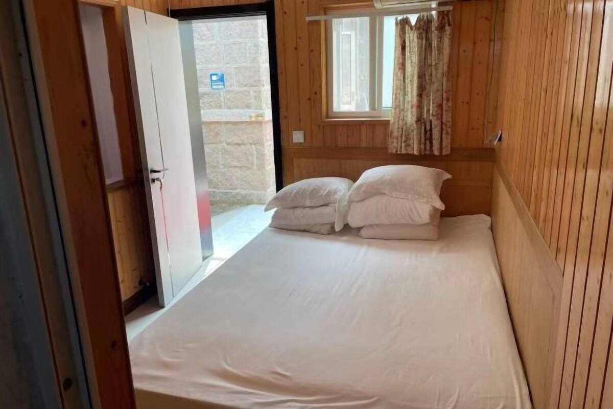 Ein Einzelbett mit weißer Bettwäsche in einem Zimmer mit Holzwänden und einem Vorhangfenster.