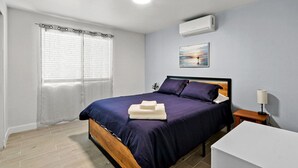 A bedroom with a bed, a bedside table, a lamp, and an air conditioning unit. - NEW! Modern 3-Bedroom Retreat Fully Updated! (El Paso)