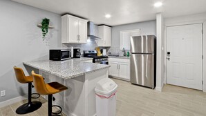 A modern kitchen with white cabinets, a stainless steel refrigerator, a microwave, and two bar stools. - NEW! Modern 3-Bedroom Retreat Fully Updated! (El Paso)