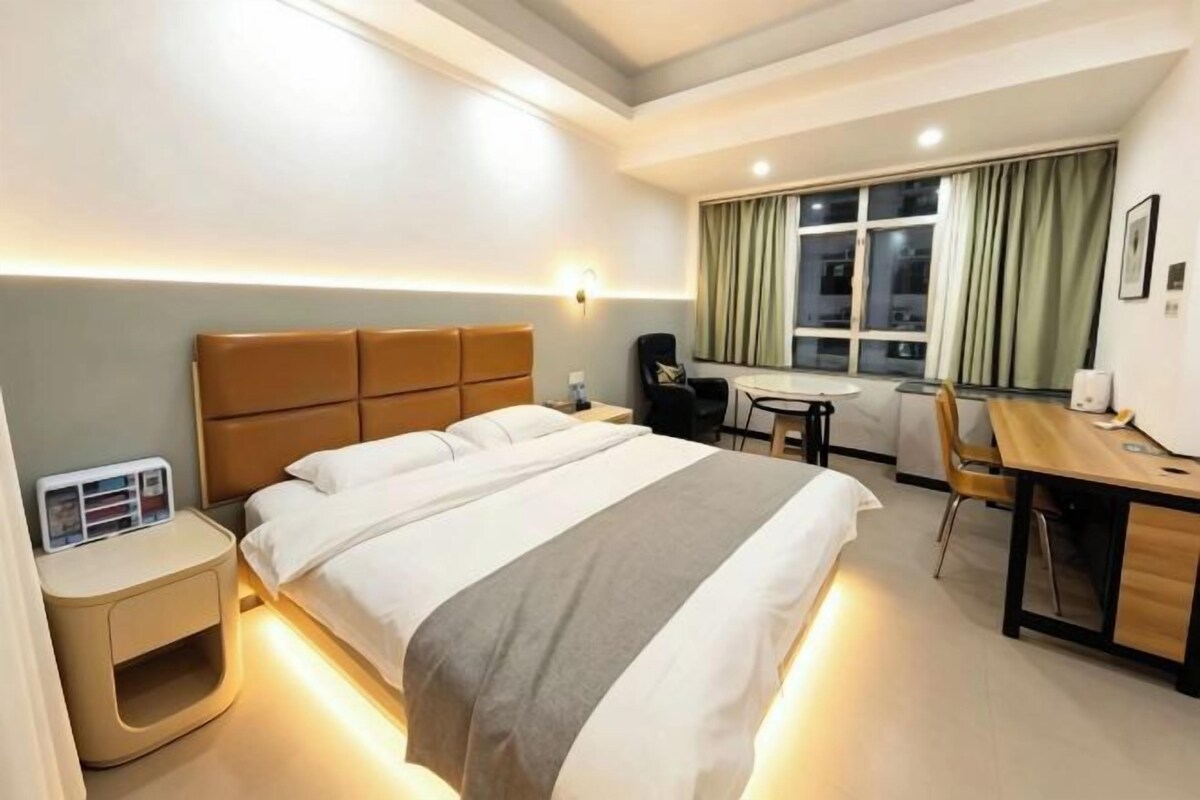 A hotel room with a bed, bedside table, desk, chair, and a window with curtains.