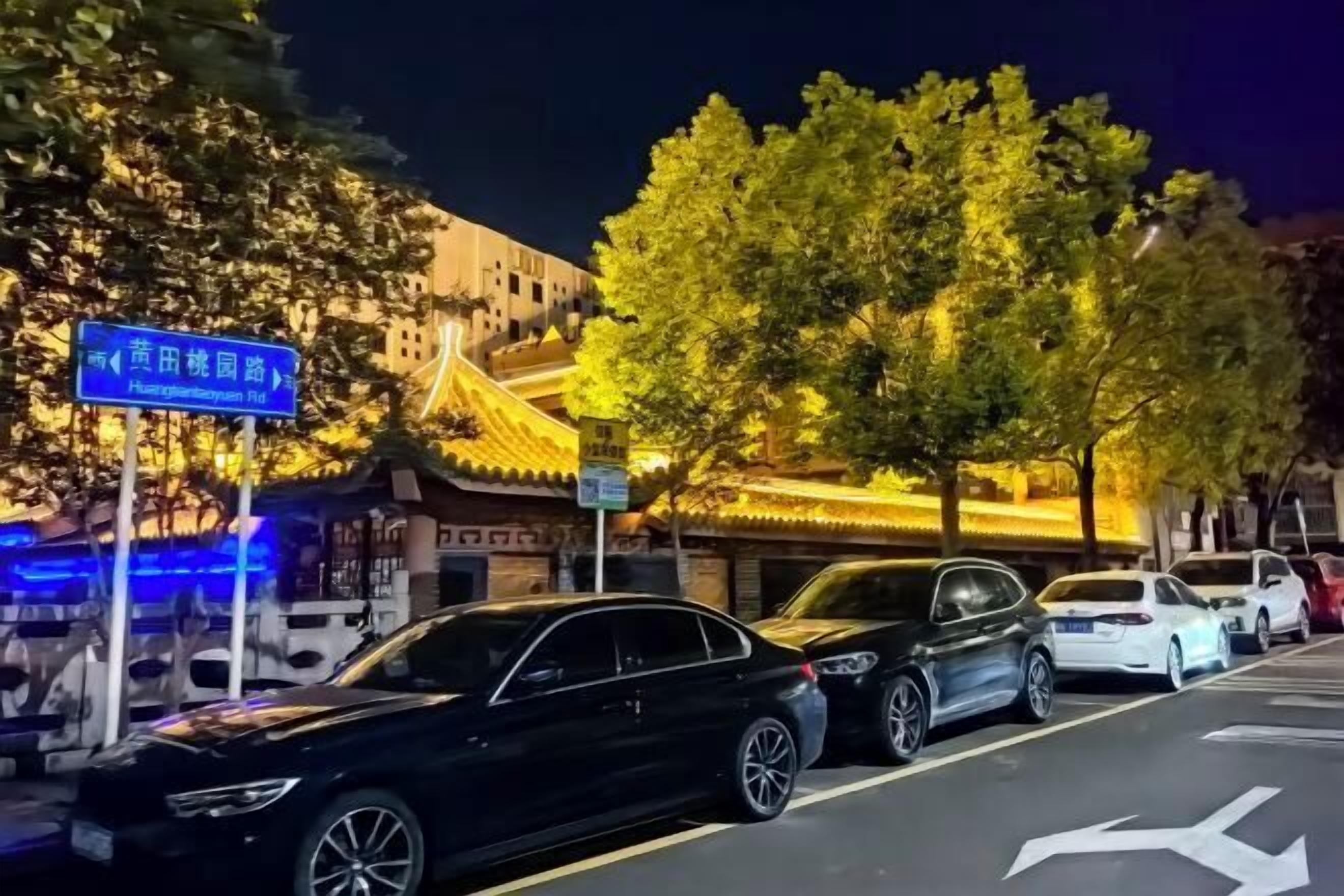 Escena urbana con coches estacionados y un edificio tradicional con letreros iluminados.