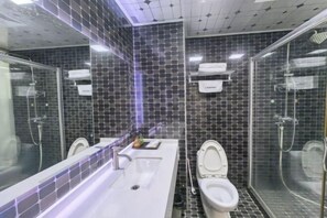 Un baño moderno con un lavamanos grande, dos inodoros y una zona de ducha con mampara de vidrio.