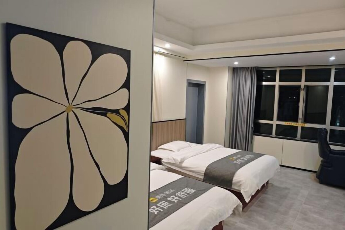 A hotel room with two beds, a large flower artwork on the wall, a window with curtains, and a chair.