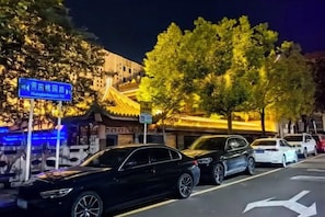 A street scene with parked cars and a traditional building with illuminated signage. - Guanglian Hotel (Shenzhen Bao'an Airport Huangtian Subway Station) (Shenzhen)