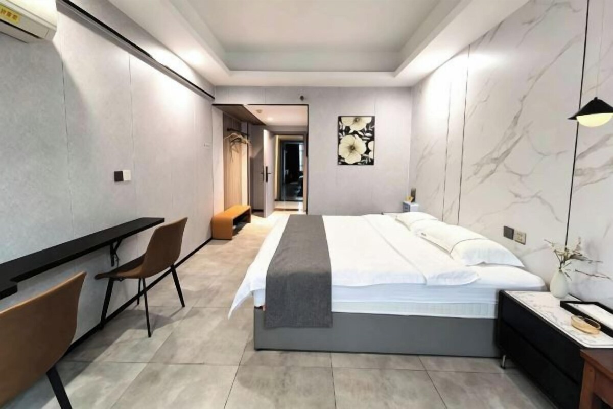 A modern hotel room with a bed, desk, chair, and a view of the hallway.