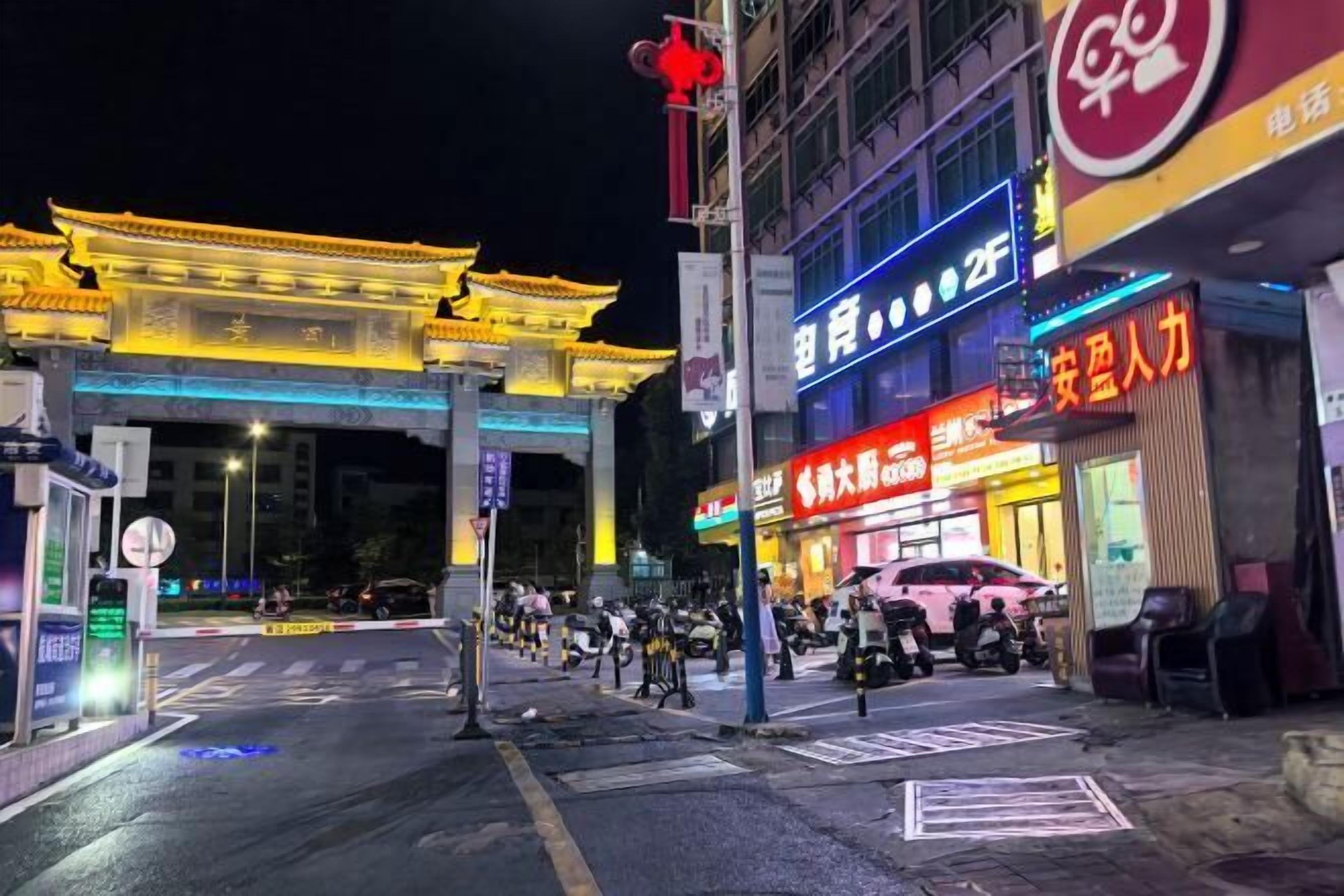 A street scene with traditional architecture, a modern building with illuminated signage, and parked vehicles.