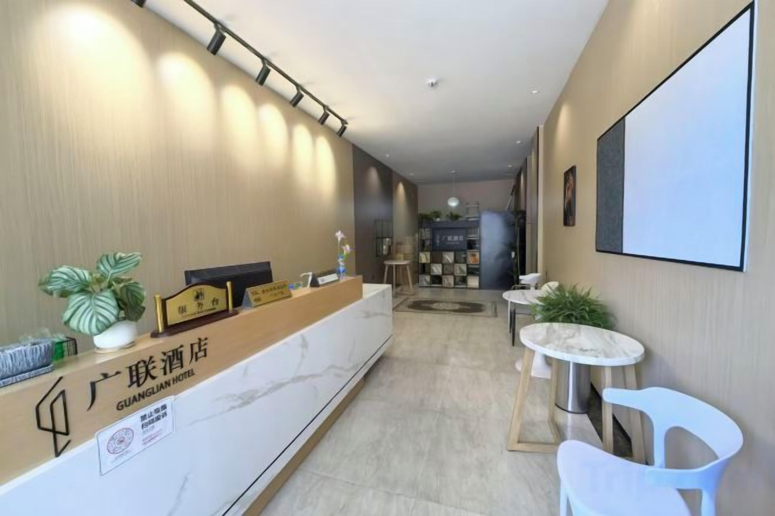 A hotel reception area with a marble counter, a reception desk, and a seating area with white chairs.