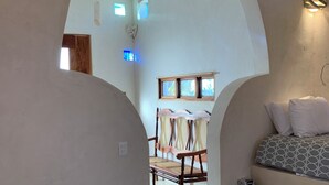 A room with a bed, a bench, and a chair. There is a window with a view of the outside. - CalleOuvert (Mérida)