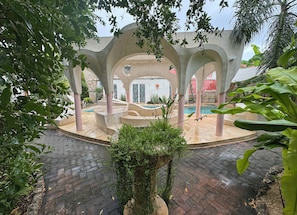A covered outdoor area with a pool, stone steps, and a view of a building in the background. - CalleOuvert (Mérida)