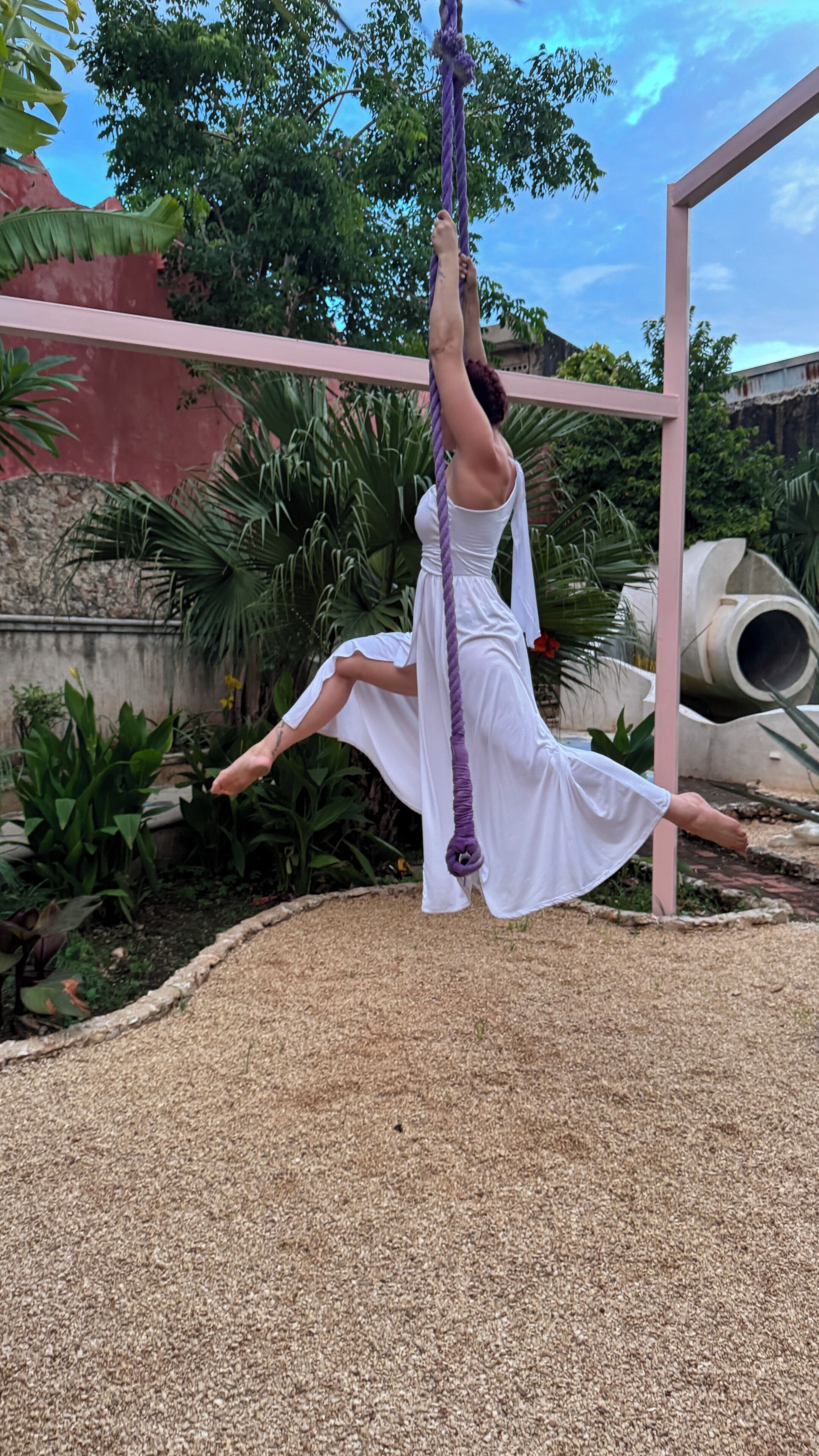 Eine Person übt Aerial Yoga an einem violetten Seil, das an einer Konstruktion befestigt ist.