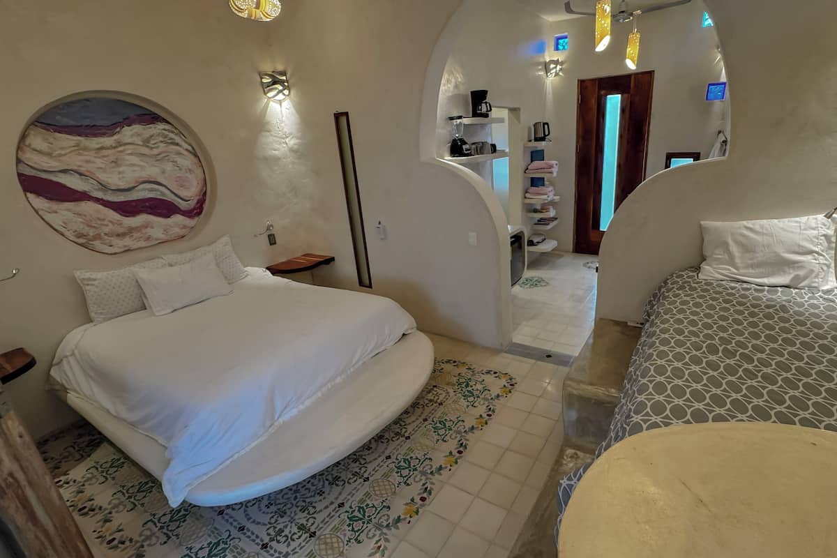 Un dormitorio con una cama grande, una cama más pequeña, una mesita de noche, una lámpara de pared y un adorno en la pared.