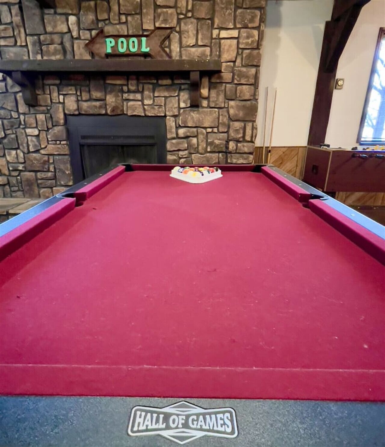 A pool table with a red felt surface, a sign above it reading "POOL", and a logo at the bottom that says "HALL OF GAMES".