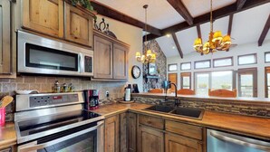A kitchen with wooden cabinets, stainless steel appliances, and a stone accent wall. - Bugle Point - Unit I1 (Ruidoso)