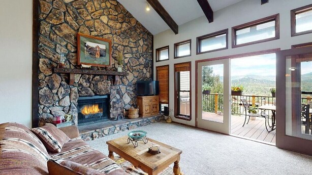 A living room with a stone fireplace, a sofa, a coffee table, and a balcony with outdoor seating. - Bugle Point - Unit I1 (Ruidoso)