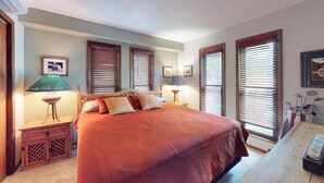 A bedroom with a large bed, wooden headboard, two bedside tables with lamps, and a wooden desk with a lamp. - Bugle Point - Unit I1 (Ruidoso)