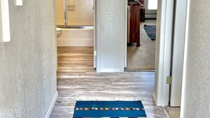 Un couloir avec un tapis à motifs, un luminaire et une porte donnant sur une salle de bain.