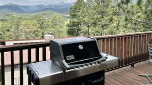 Un barbecue Weber Spirit sur une terrasse en bois, avec vue sur les montagnes et les arbres.