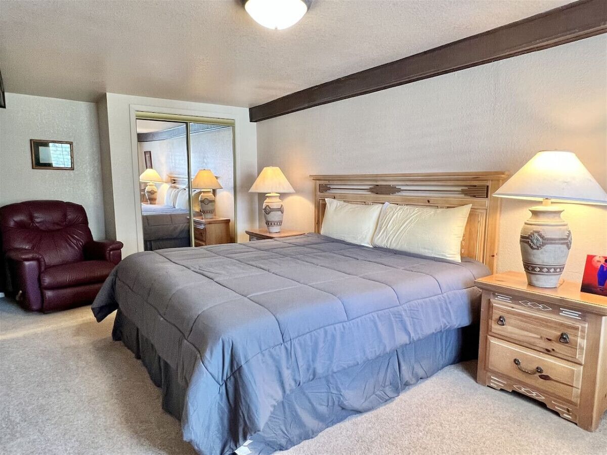 A bedroom with a bed, a nightstand, a lamp, a chair, and a mirror.