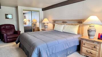 A bedroom with a bed, a nightstand, a lamp, a chair, and a mirror.