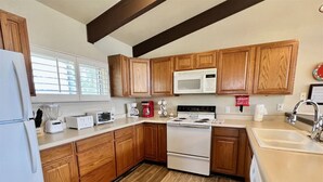 Une cuisine avec des meubles de rangement en bois, un réfrigérateur blanc, un four à micro-ondes, une cuisinière et un évier.