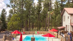 A swimming pool surrounded by stone walls, with red umbrellas and lounge chairs.
