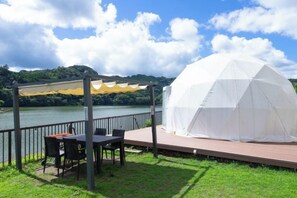 Ein Pavillon mit Tisch und Stühlen, einem weißen Zelt und Blick auf einen See.