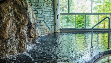 An indoor swimming pool with stone walls and a view of greenery outside.