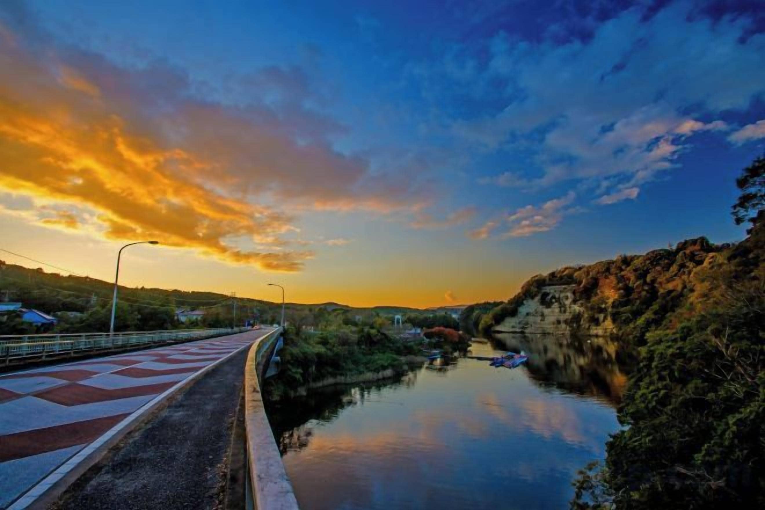A river with a bridge, surrounded by greenery and a sunset sky.