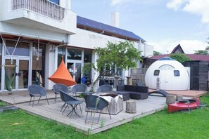 Ein modernes Haus mit einer Terrasse, Sitzgelegenheiten im Freien und einer ungewöhnlichen, kugelförmigen Struktur.