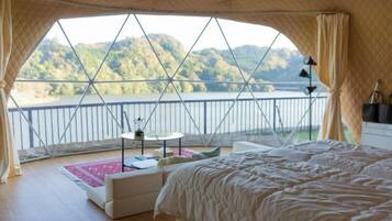 A bedroom with a large bed, a small table, and a view of a lake and mountains.