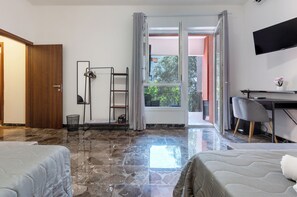 A hotel room with a bed, a desk, a chair, a TV, a window with curtains, and a balcony. - Hesa House (Cagliari)