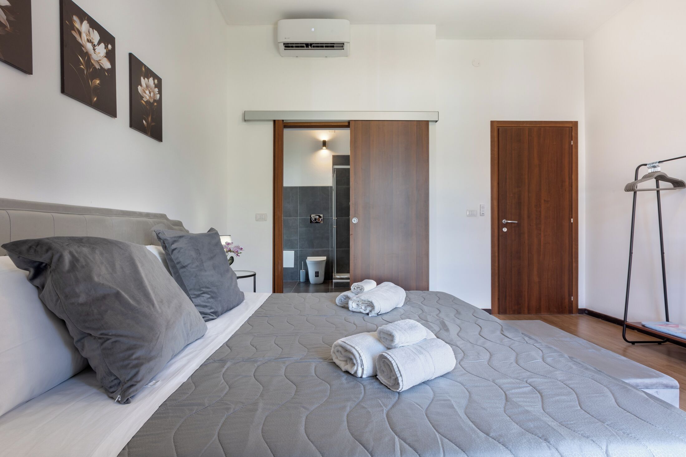 Quarto com cama, travesseiros, toalha, porta e ar-condicionado fixado na parede.