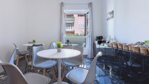 Habitación de hotel con zona de comedor que incluye una mesa redonda y sillas, una planta pequeña en maceta y vistas a un balcón exterior a través de una puerta abierta.