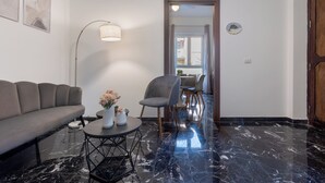 Una sala moderna con un sofá, una mesa redonda de centro con jarrones, una lámpara de pie y vistas a otra habitación a través de una puerta.